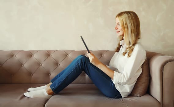 Modern young woman working with digital tablet computer, interested girl watching video on a tablet sitting on the couch in living room at home