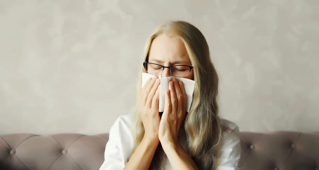 Sick exhausted middle aged woman sneezing blow nose using tissue at home