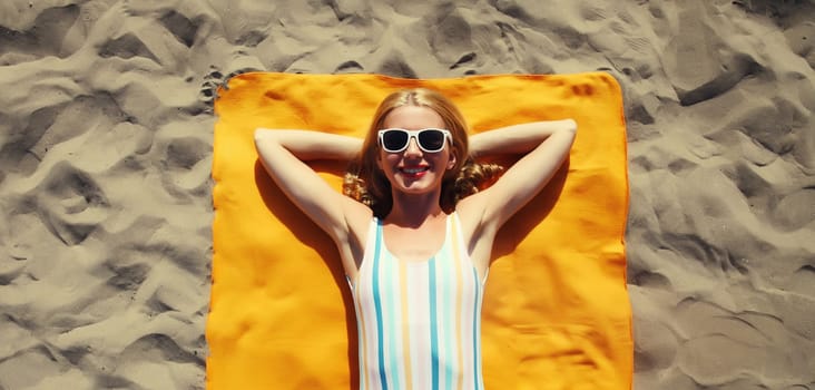 Summer vacation, happy relaxing young woman lying on sand on the beach, girl smiling lying on beach towel top view, wearing swimsuit, glasses
