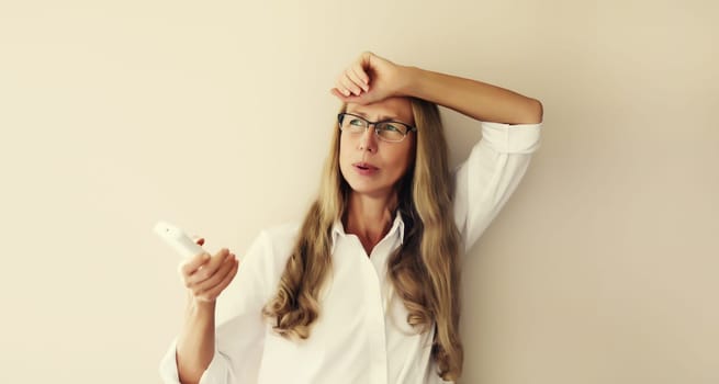 Exhausted woman turns on the air conditioner, suffering from heat, hot weather, high temperature, girl with breathing difficulties in the room using the remote control at home