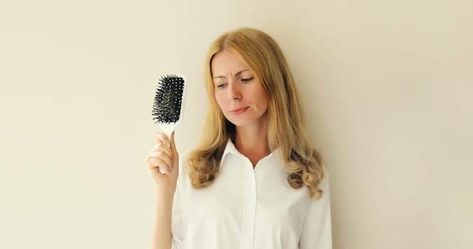 Unhappy disappointed young woman with hair loss condition, showing hair brush, blonde caucasian girl with unhealthy hair standing on white background