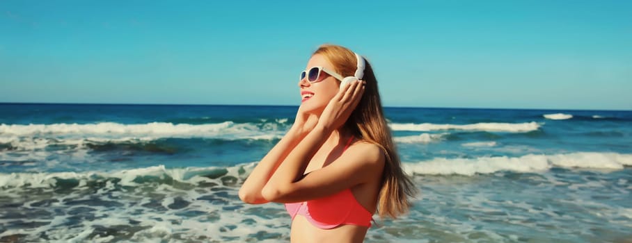 Summer vacation of relaxed happy young woman enjoying listening to music with headphones on the beach at sea coast on a sunny day