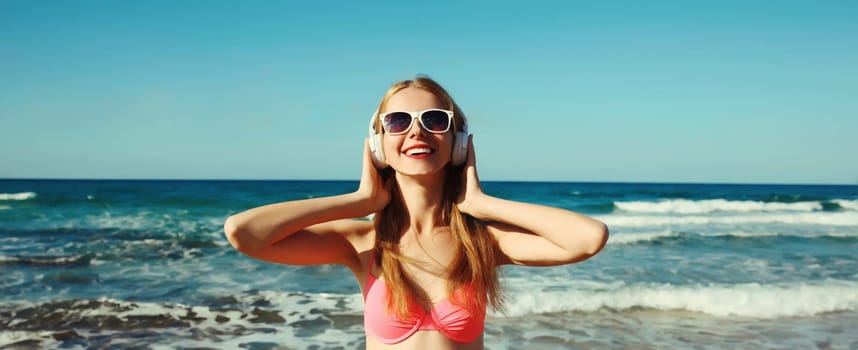 Summer vacation of happy smiling young woman relaxing listening to music with headphones on the beach at sea coast on a sunny day