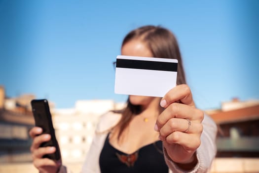 Happy young woman with glasses holding in each hand a credit card and telephone Looking into the camera. Concept: payment in an online store