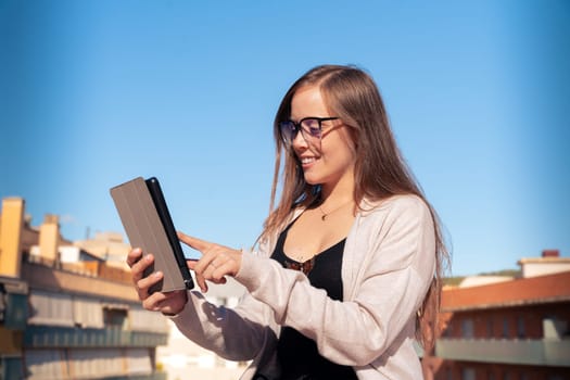 Beautiful young adult caucasian woman with glasses typing on tablet pc happy