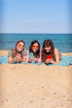 Group of smiling multiethnic women enjoying vacation. Beautiful and cheerful Gen Z girls with their mobile phones pose looking at the camera with a mobile phone.