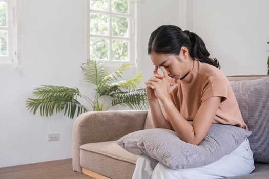 Young woman feeling sick with a headache, sitting on a couch at home, holding her head in her hands, experiencing pain and discomfort.