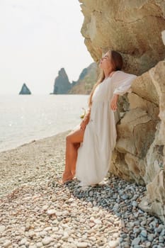 woman white dress standing on a beach, looking out at the ocean. She is lost in thought, with her hand on her hip. Concept of calm and introspection