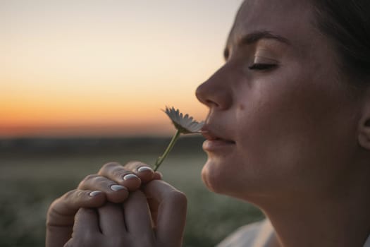 A woman is smelling a flower. The flower is white and the woman is looking away