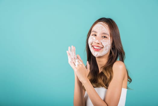 Portrait Asian young woman hands are adorned with white foam cleaning face studio shot isolated on blue background, beautiful female holds a cleansing foam on palm, Cosmetics beauty skincare