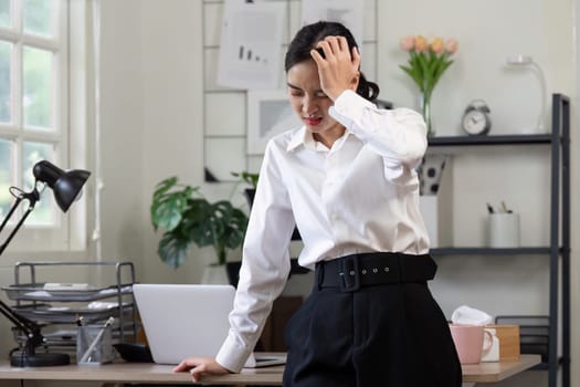 A businesswoman experiencing a headache while working in an office, illustrating the concept of workplace stress and overwork.