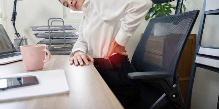 Business professional suffering from back pain while working at an office desk, highlighting workplace health and ergonomics.