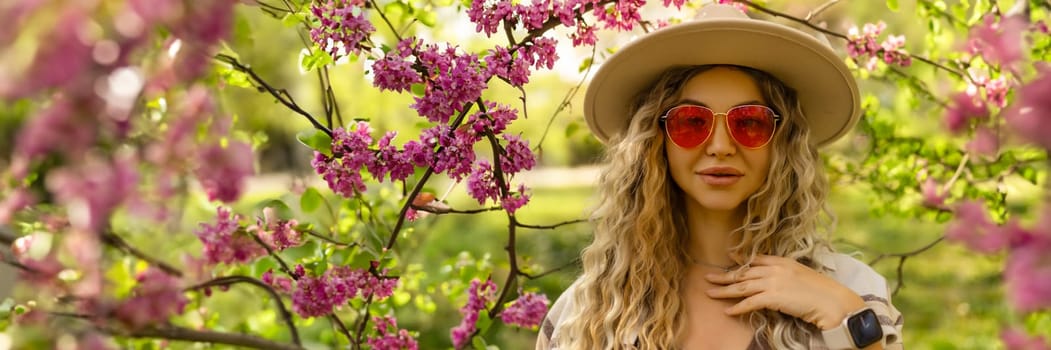 Beautiful woman in sunglasses near blossoming tree on spring day, space for text banner.