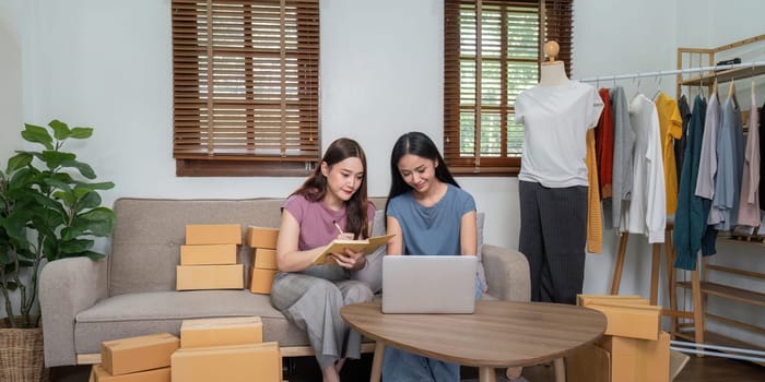 Lesbian couple working from home, managing their online clothing business, packing orders, and using a laptop for inventory management.