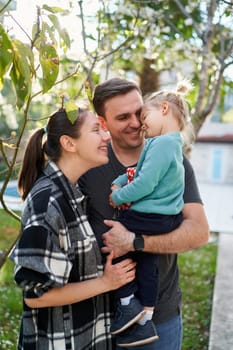 Smiling mother looking at little girl sitting in dad arms hugging her in the garden. High quality photo