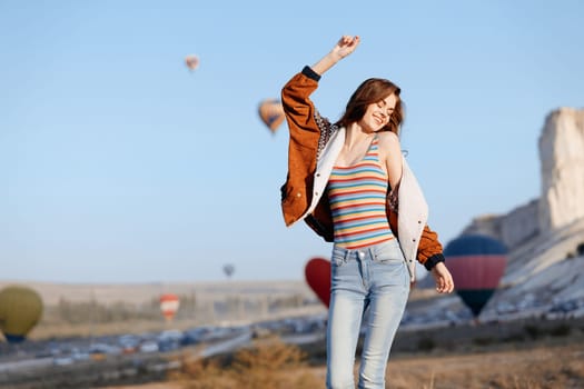 joyful woman leaping with striped shirt as colorful hot air balloons float in the sky