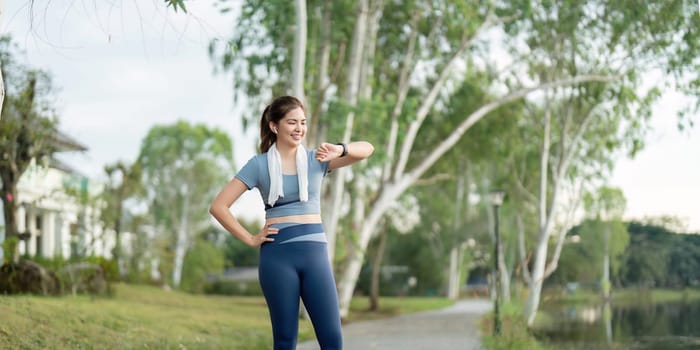 A woman checks her watch during a morning run in a scenic park, surrounded by lush greenery and a tranquil atmosphere.