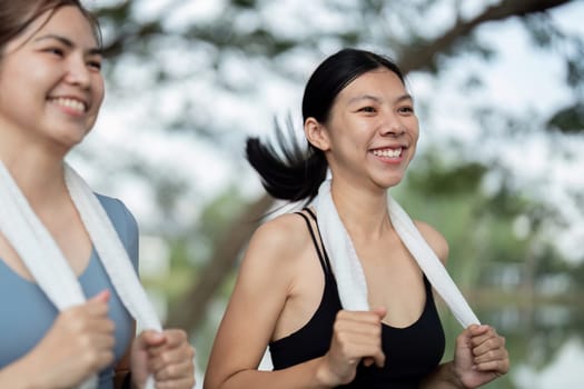 Two friends jogging in the morning, smiling and enjoying their exercise routine with towels around their necks in a lush park.