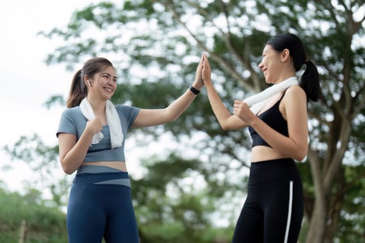 Two women in athletic wear high fiving after a morning run, celebrating their exercise routine in an outdoor park.