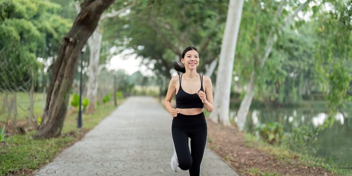 A young woman in athletic wear jogging on a path in a beautiful park during the morning, surrounded by lush trees and a calm lake.