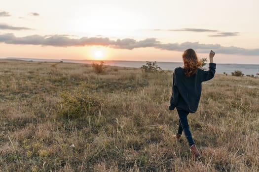 tranquil sunset stroll woman with outstretched arms and windblown hair in field at dusk