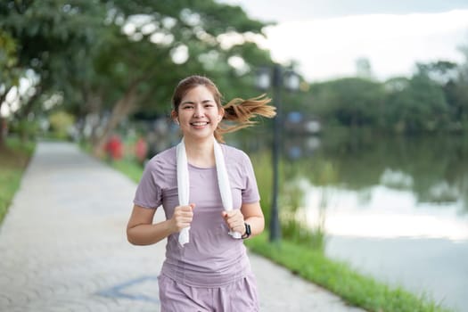 A young woman running in the morning along a scenic lakeside path, smiling and enjoying her exercise routine.