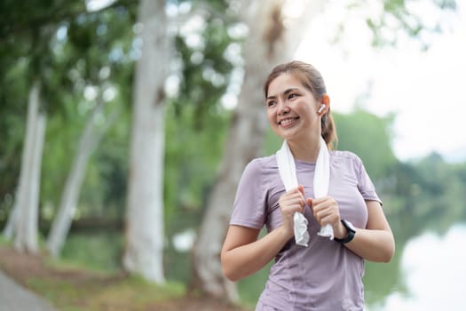 A woman enjoying her morning run in a park, smiling and wearing sports attire with a towel around her neck, surrounded by trees and nature.