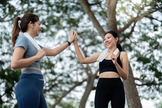 Two women high fiving and smiling after a morning run in the park, celebrating their fitness achievements and enjoying a healthy lifestyle.
