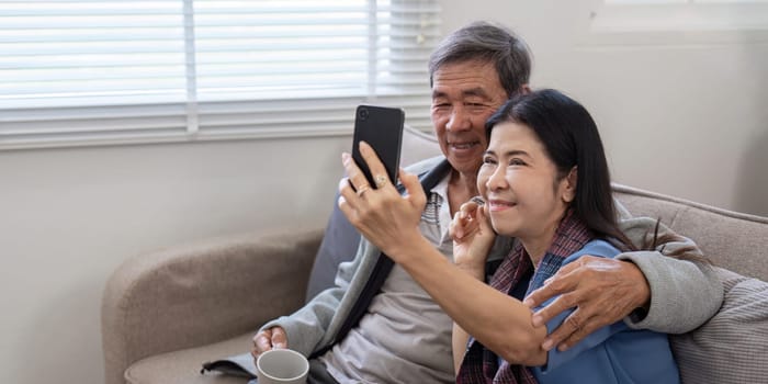 An elderly couple taking a selfie together at home, showcasing their love and companionship in a cozy living room setting.