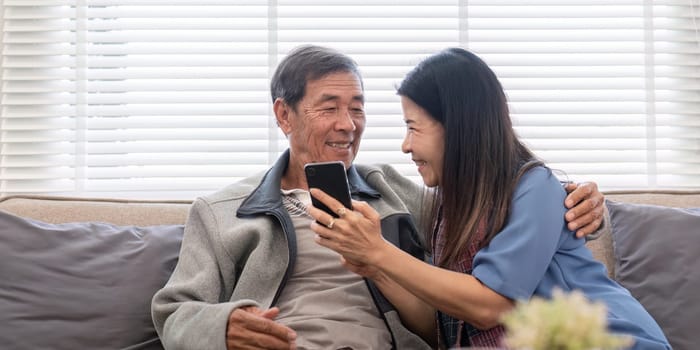 An elderly couple happily using a smartphone together, exploring online shopping and social media in a cozy home setting.