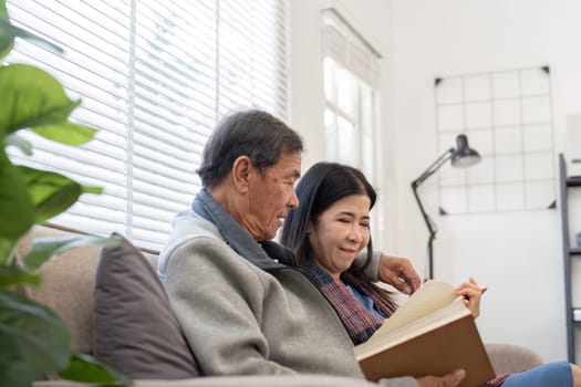 An elderly couple sits together on a sofa, sharing a book and enjoying each others company in a bright, modern living room.