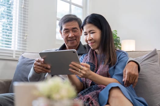 An elderly couple sitting together on a couch, sharing a moment of joy while using a tablet in a bright and cozy living room.