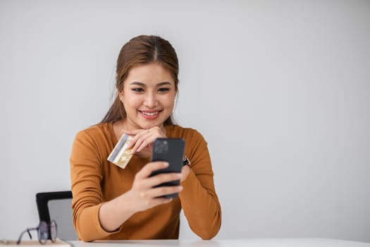 A woman happily uses her credit card and smartphone to shop online, showcasing the convenience of modern technology in a minimalist setting.