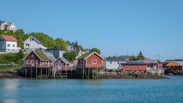 A scenic view of Reine, Lofoten, Norway, waters edge, with a clear blue sky and calm waters in the background.