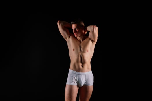 Man holds barbell weights, young adult strong male in a white briefs, studio shot. Sport and muscles.