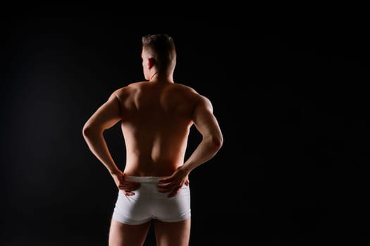 Man holds barbell weights, young adult strong male in a white briefs, studio shot. Sport and muscles.