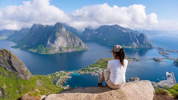 A lone traveler enjoys the breathtaking view from a mountaintop overlooking the turquoise waters and rugged landscapes of the Lofoten Islands in Norway. Reinebringen, Lofoten, Norway