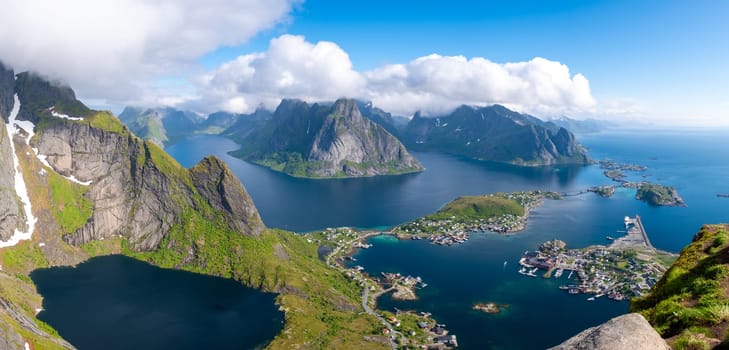 A panoramic view of the Lofoten Islands in Norway, showcasing the dramatic mountain peaks, turquoise fjords, and a small village nestled amongst the rugged landscape. Reinebringen, Lofoten, Norway