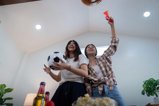 Lesbian couple celebrating a football victory at home, showing excitement and joy. Perfect for themes of love, sports, and modern relationships.