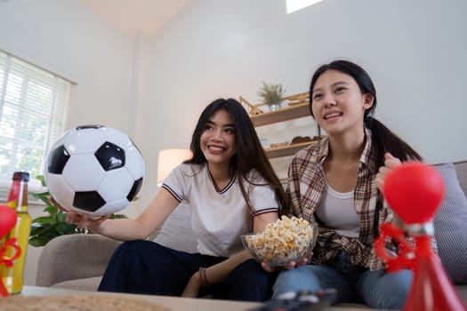 Happy lesbian couple enjoying a football match together at home, cheering and celebrating with snacks and drinks.