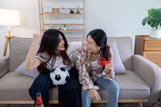 Happy lesbian couple celebrating a football victory together on a cozy sofa, showcasing love, joy, and unity.