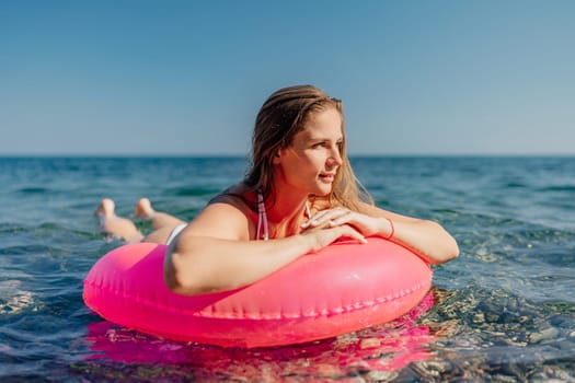 A woman is laying on a pink inflatable ring in the ocean. The scene is peaceful and relaxing, with the woman enjoying the water and the sun