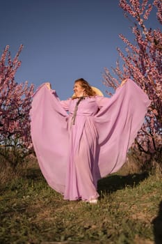 Woman blooming peach orchard. Against the backdrop of a picturesque peach orchard, a woman in a long pink dress and hat enjoys a peaceful walk in the park, surrounded by the beauty of nature