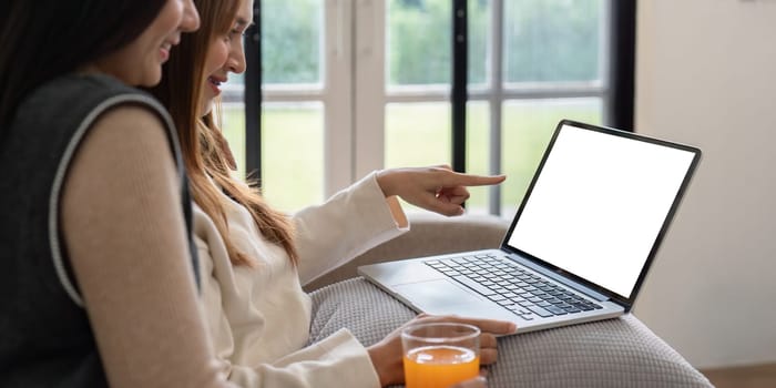 Lesbian couple sitting on a couch, using a laptop with a blank screen, enjoying a relaxed moment at home. Perfect for tech, lifestyle, and LGBTQ themes.