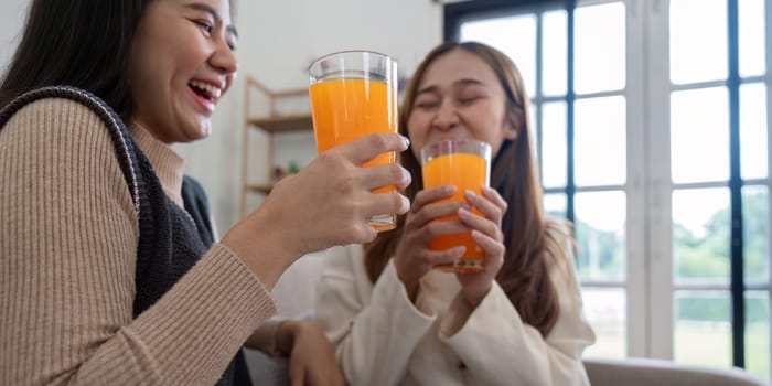 Two smiling women share a moment of joy while drinking healthy orange juice in a cozy, sunlit home environment.