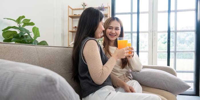 A joyful lesbian couple sitting on a couch, drinking fresh orange juice in a bright, modern home setting, promoting healthy living and love.