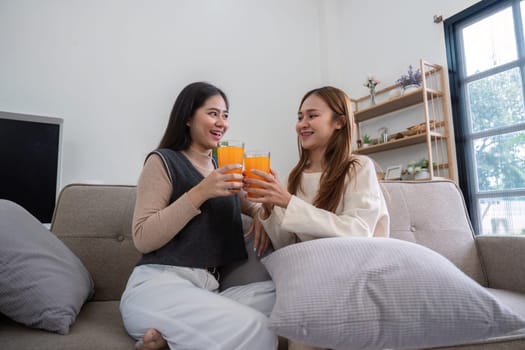 A joyful lesbian couple sitting on a couch, clinking glasses of fresh orange juice in a bright and modern living room.