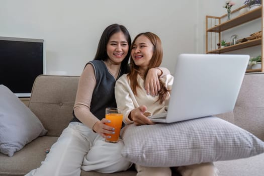 Happy lesbian couple drinking orange juice and relaxing at home with a laptop, enjoying a healthy lifestyle and quality time together.