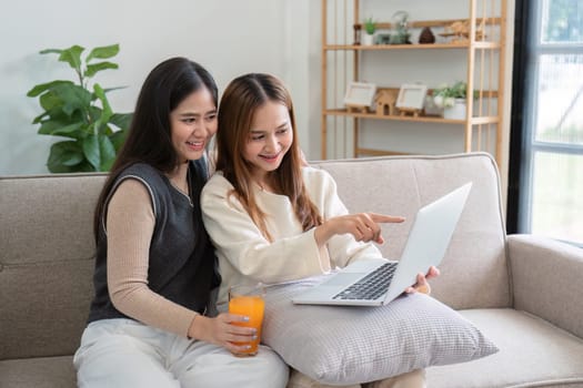 A cheerful lesbian couple drinks healthy orange juice at home, enjoying a relaxing moment together on the couch.