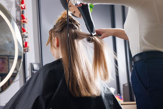 hairdresser drying hair with hair dryer and comb in beauty salon, drying hair close up, self care concept